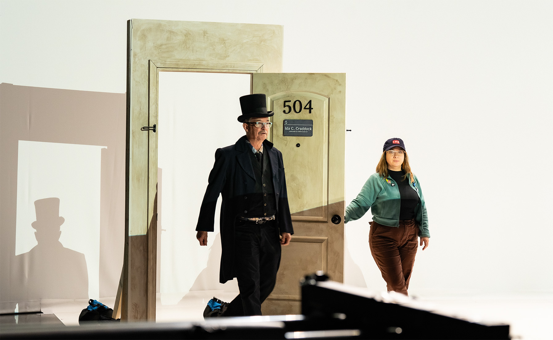 Man in top hat walking through a door held open by crew member