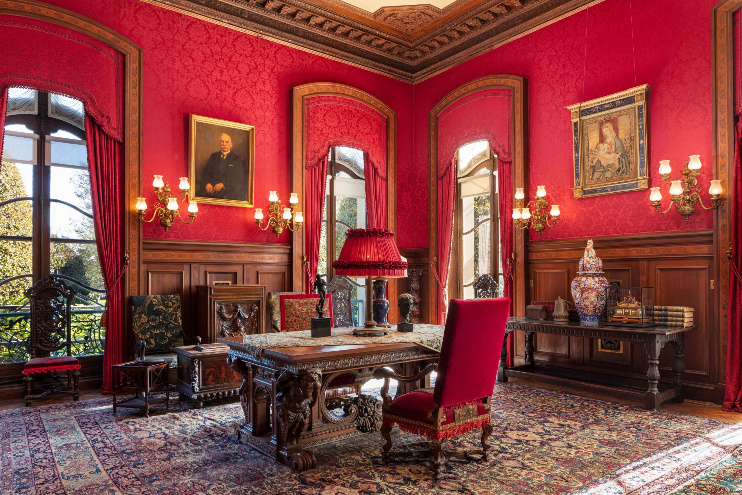 Ornate table centered in a wood-paneled room with red wallpaper and curtains