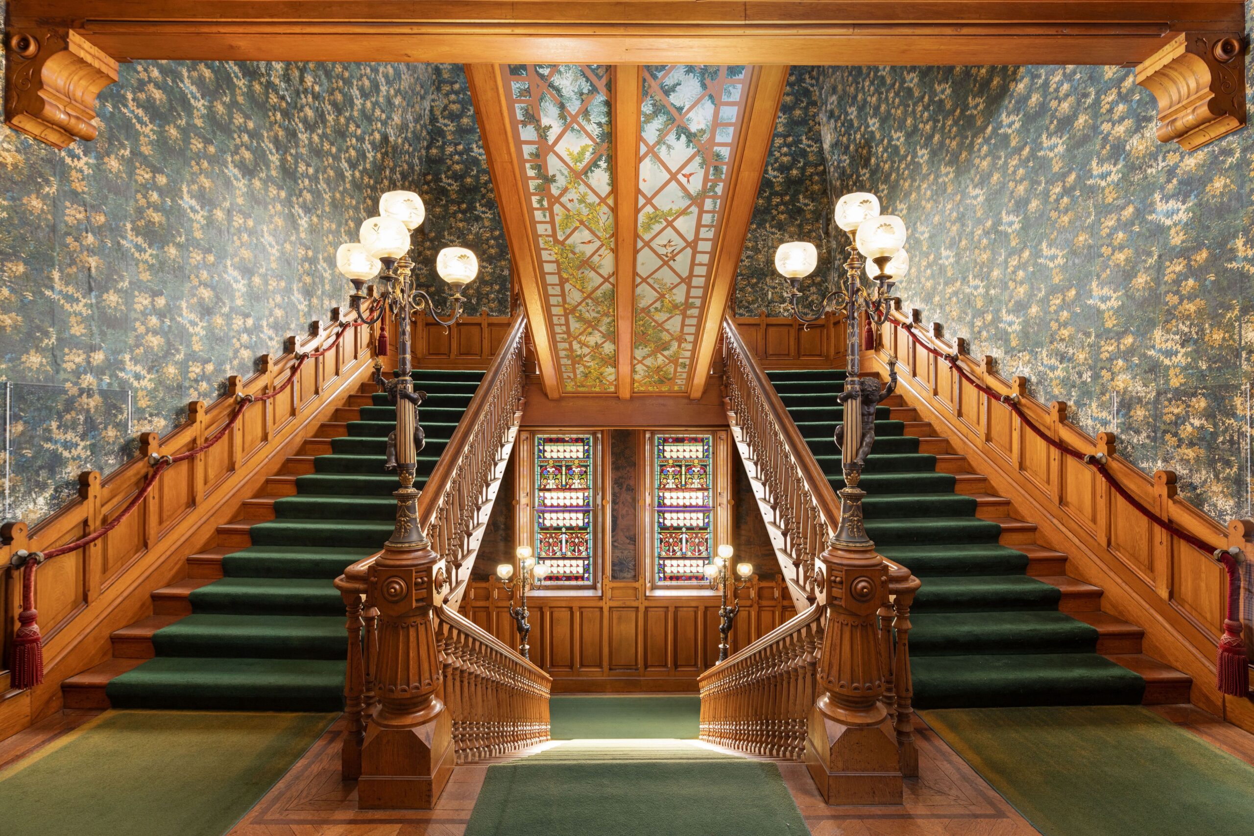 Symmetrical ornate wood staircases with green carpeting and wallpaper