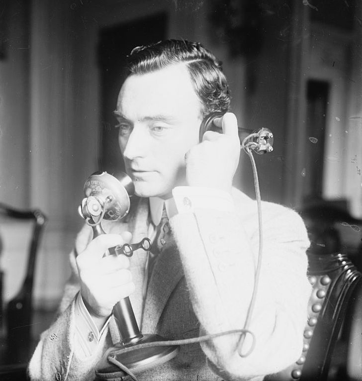 Black and white photograph of John Purroy Mitchel, using an upright telephone, facing away from the camera