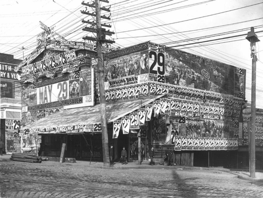Black and white photograph of a building covered in posters advertising the Ringling Brothers